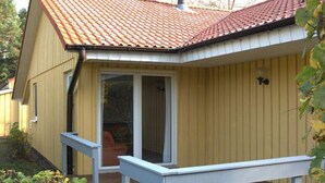 Eine Holzterrasse mit überdachtem Bereich, einer Schiebetür und einer kleinen Sitzgelegenheit im Freien.