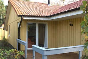 Eine Holzterrasse mit überdachtem Bereich, einer Schiebetür und einer kleinen Sitzgelegenheit im Freien.
