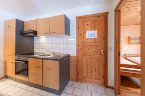 A compact kitchen with wooden cabinets, a stove, and a sink. - Gemütlich eingerichteter Doppelbungalow mit Garten in Mirow (Granzow)