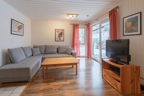 A living room with a grey sofa, wooden coffee table, and a television on a wooden stand. - Gemütlich eingerichteter Doppelbungalow mit Garten in Mirow (Granzow)