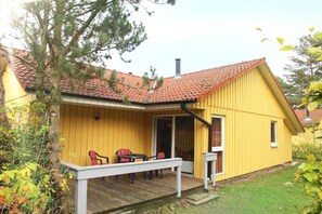 A yellow building with a red-tiled roof, a covered patio with chairs, and a small window. - Gemütlich eingerichteter Doppelbungalow mit Garten in Mirow (Granzow)