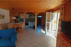 A wooden interior with a dining area, kitchen, and a TV on a wooden cabinet. - Schöner Doppelbungalow mit Terrasse und Garten in Mirow (Granzow)