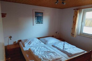 A bedroom with a bed, a nightstand, a wall-mounted lamp, a window with curtains, and a painting on the wall. - Schöner Doppelbungalow mit Terrasse und Garten in Mirow (Granzow)