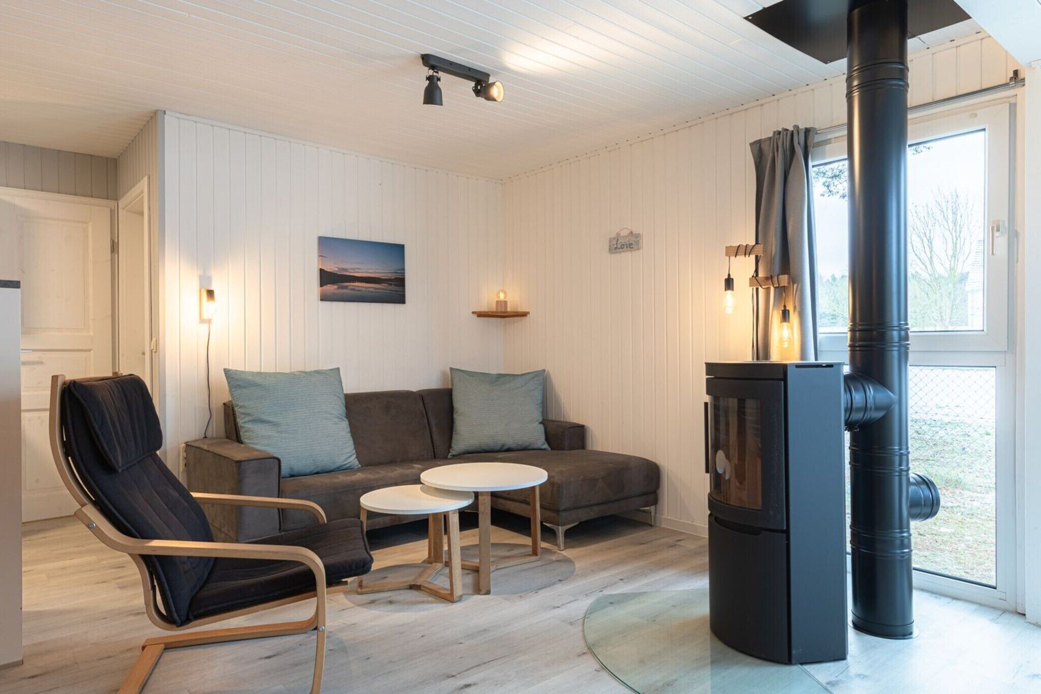 Una sala de estar acogedora con sofá, dos sillones, una mesita, chimenea y ventana con cortinas.