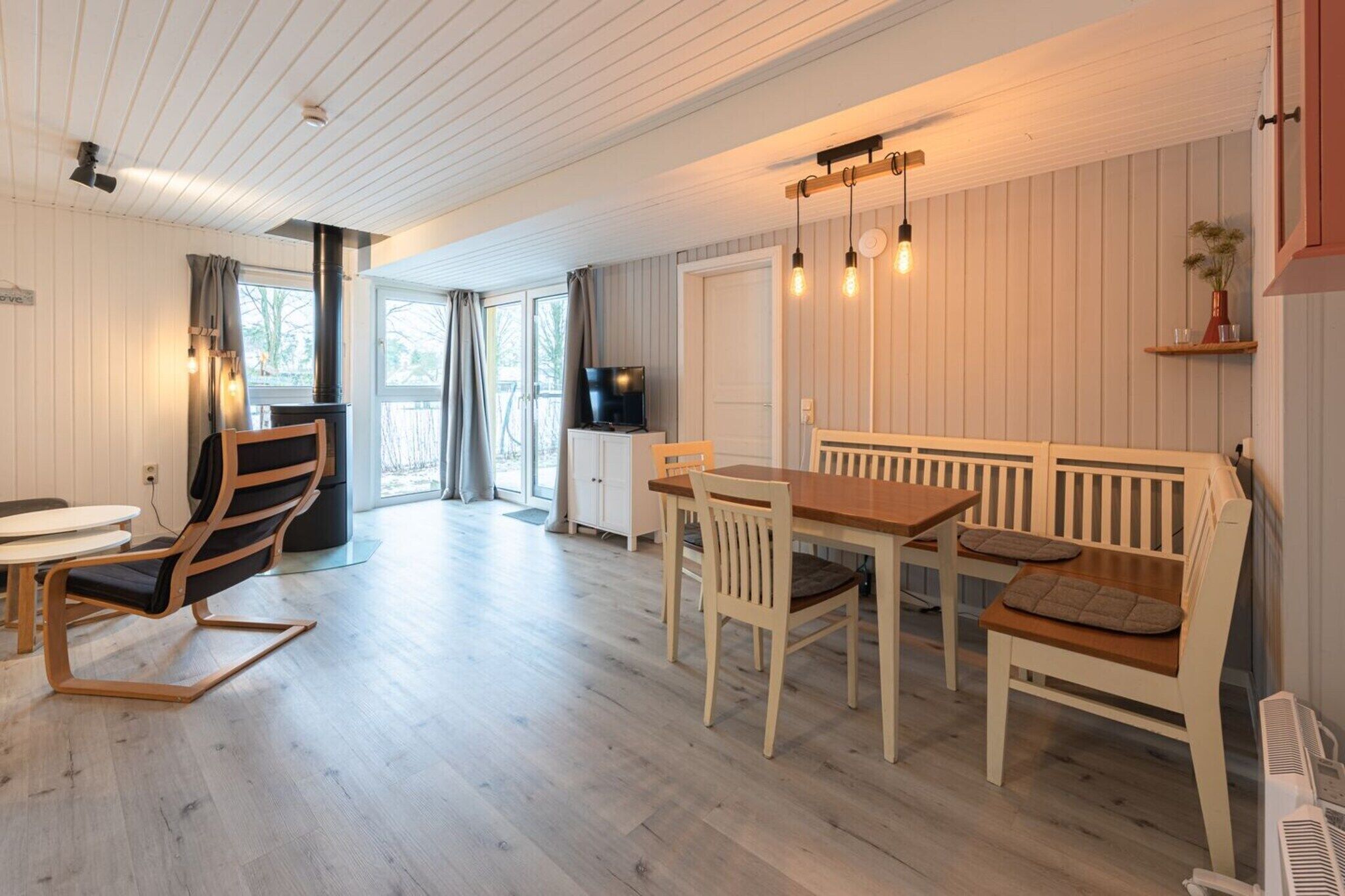 Un intérieur moderne avec une table à manger en bois, des bancs blancs, un téléviseur et une cheminée.