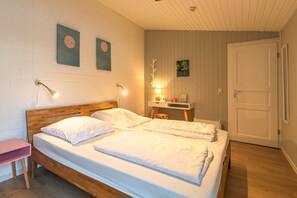 A bedroom with a wooden bed, bedside lamps, a small table, and a door. - Modern eingerichteter Doppelbungalow mit Garten in Mirow (Granzow)