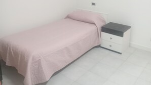Ein Einzelbett mit weißem Kopfteil und einem kleinen Nachttisch mit Schubladen.