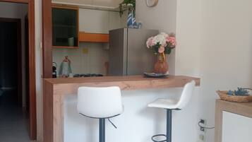 A modern kitchen with a wooden island, two bar stools, a refrigerator, and a clock on the wall.