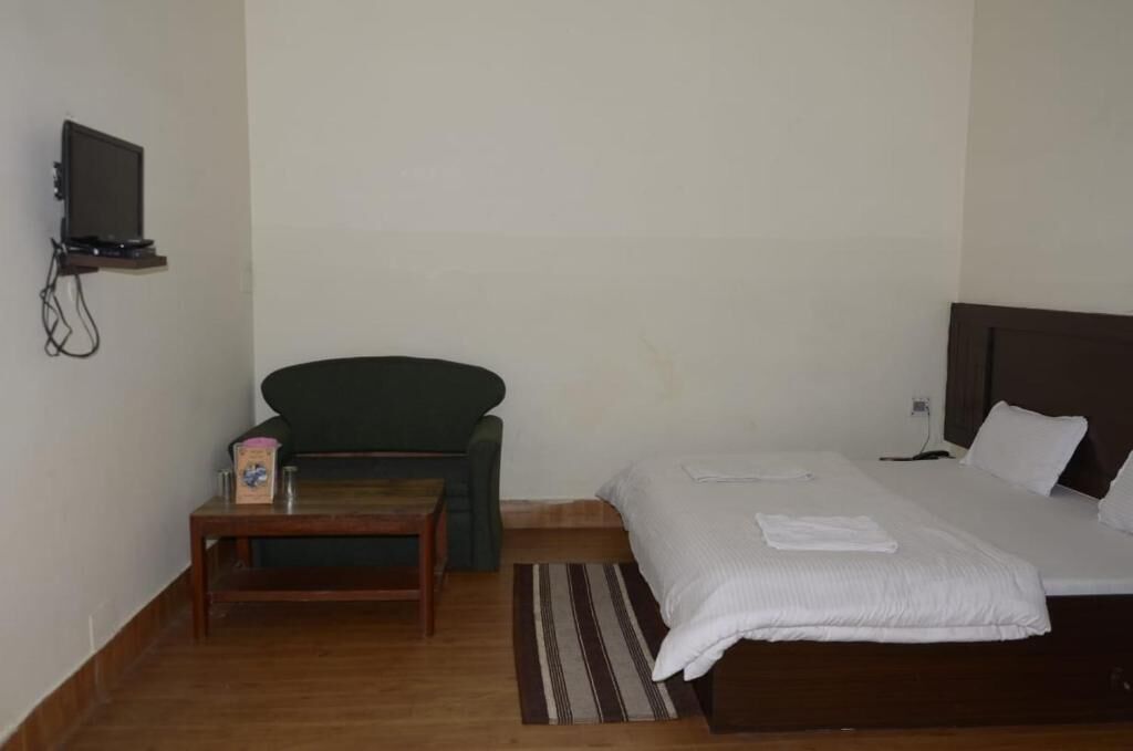A room with a bed, a small table, a chair, a television mounted on the wall, and a bedside table.