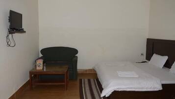 A room with a bed, a small table, a chair, a television mounted on the wall, and a bedside table.