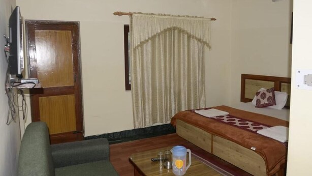 Una habitación con cama, una mesita con jarrón, televisión y puerta.