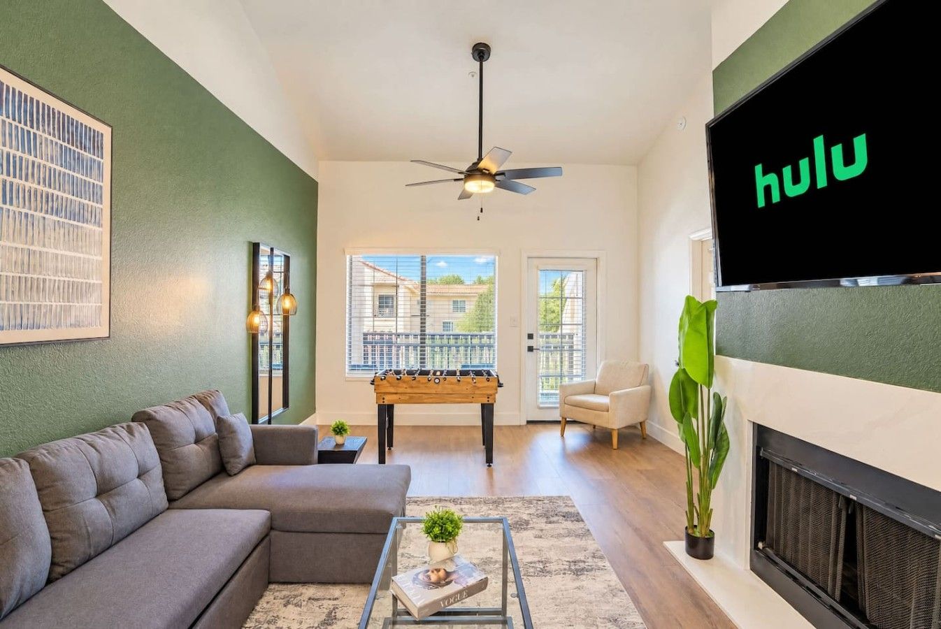 A living room with a sofa, a coffee table, a foosball table, a television, and a fireplace.