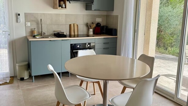 A modern kitchen with a dining area, including a round table and four chairs, a built-in oven, and a view through a glass door. - Les 4 Sources / Apartment with a view, terrace, air conditioning, and private parking (Villelaure)