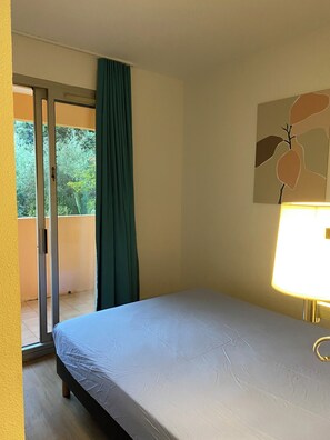Ein Hotelzimmer mit Bett, Fenster mit Vorhängen, Tür und Wand mit einem Gemälde.