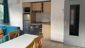 Uma cozinha compacta com geladeira, fogão, pia e lava-louças. Há uma área de refeições com mesa e cadeiras.