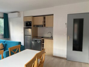 Eine kompakte Küche mit Kühlschrank, Herd, Spüle und Geschirrspüler. Es gibt einen Essbereich mit Tisch und Stühlen.