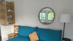 A room with a teal sofa, a wooden chair, a small table, a mirror, and a lamp.