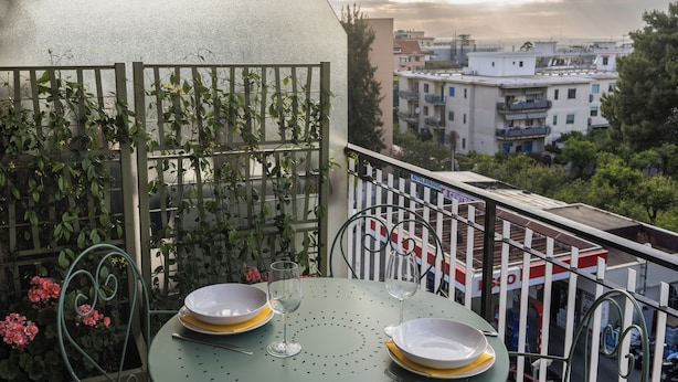A balcony with a table set for two, a metal railing, and a view of buildings in the background. - ErKaNi Dimora Sorrento – Contemporary 1-Bedroom Apartment in Downtown Sorrento (Sorrento)