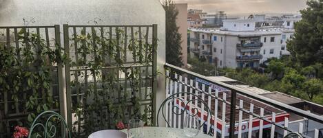 A balcony with a table set for two, a metal railing, and a view of buildings in the background.