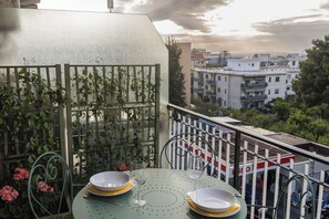 A balcony with a table set for two, a metal railing, and a view of buildings in the background. - ErKaNi Dimora Sorrento – Contemporary 1-Bedroom Apartment in Downtown Sorrento (Sorrento)