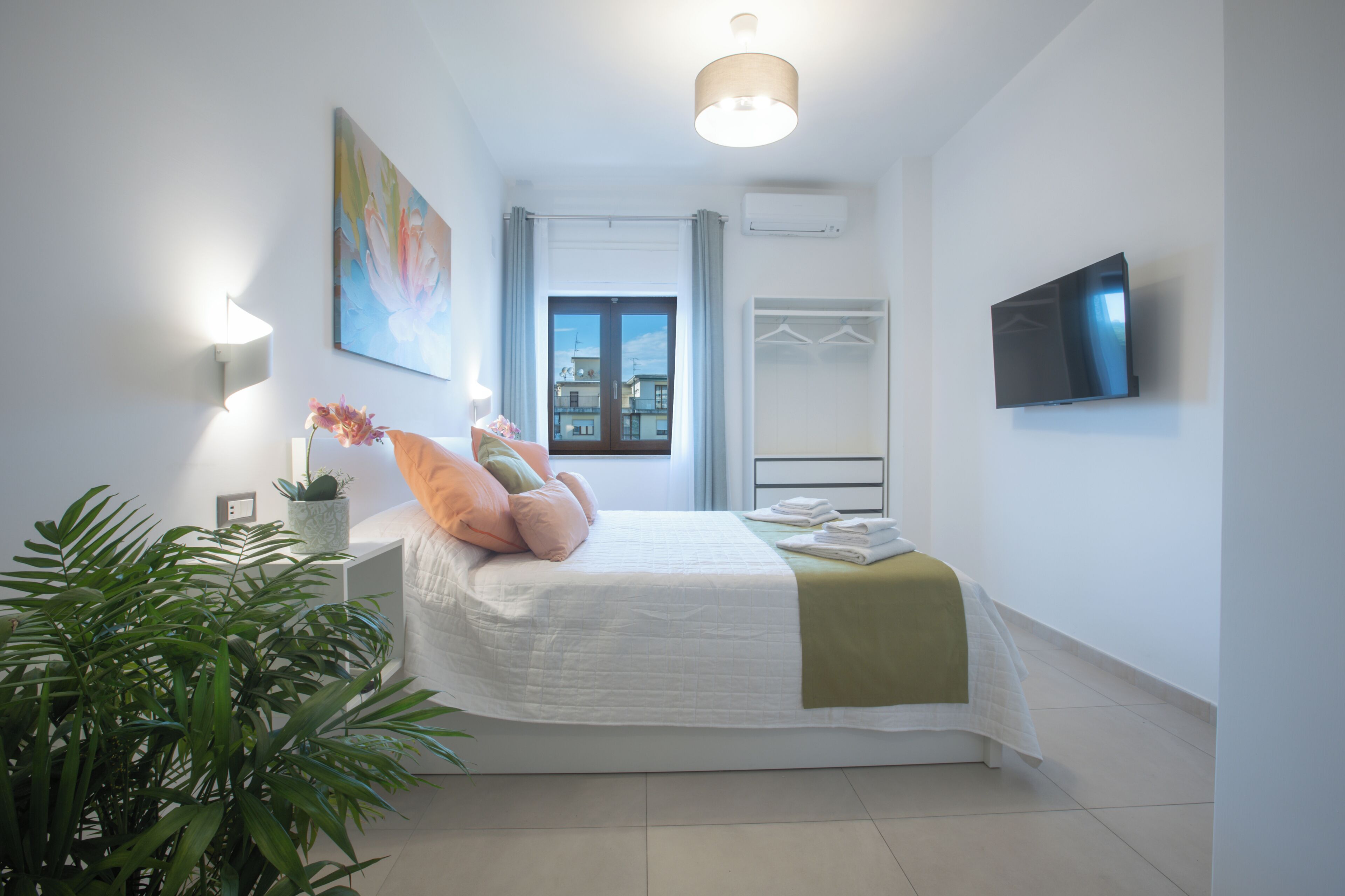 A modern bedroom with a bed, bedside lamps, a TV, and a window with a view.