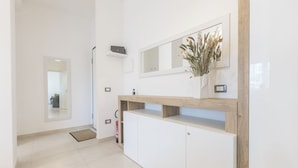A modern interior with a white reception desk, a mirror, a vase with dried flowers, and a fire extinguisher. - ErKaNi Dimora Sorrento – Contemporary 1-Bedroom Apartment in Downtown Sorrento (Sorrento)