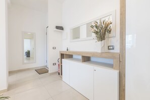 A modern interior with a white reception desk, a mirror, a vase with dried flowers, and a fire extinguisher. - ErKaNi Dimora Sorrento – Contemporary 1-Bedroom Apartment in Downtown Sorrento (Sorrento)