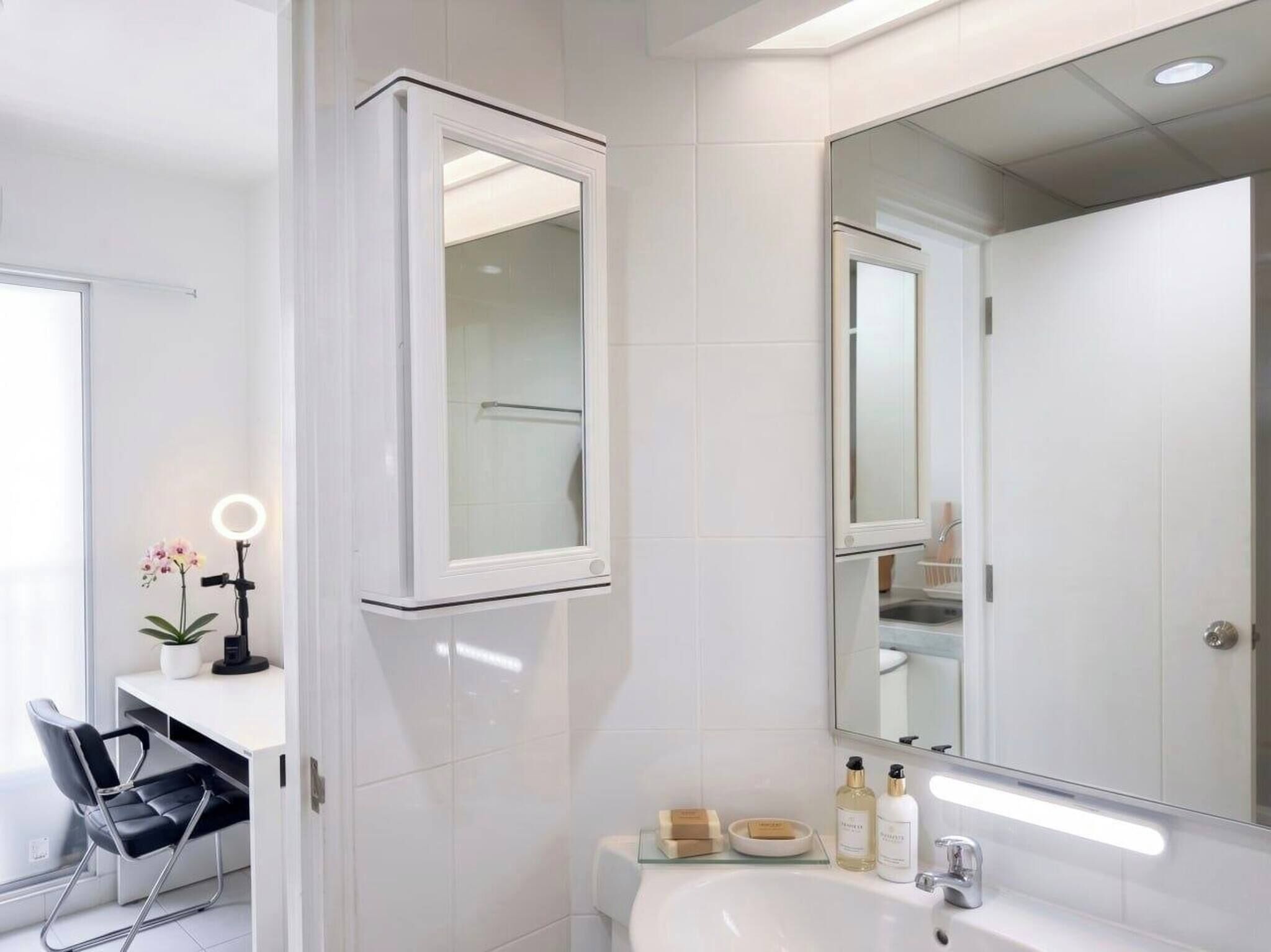 A modern bathroom with a large mirror, white tiles, a sink, and a chair.