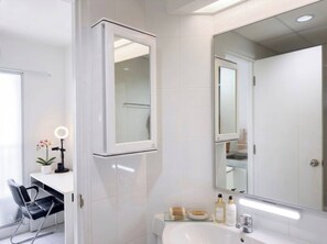 Ein modernes Badezimmer mit großem Spiegel, weißen Fliesen, einem Waschbecken und einem Sessel.