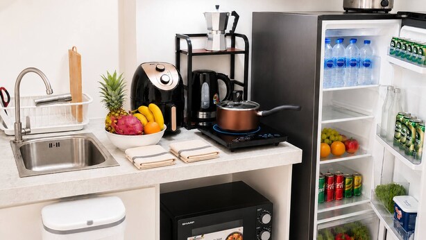 A compact kitchen with a sink, a coffee maker, a kettle, a microwave, and a refrigerator stocked with beverages and snacks. - S&G Beachfront Serviced 1-br, Step to Tops and 7-11 (Pattaya)