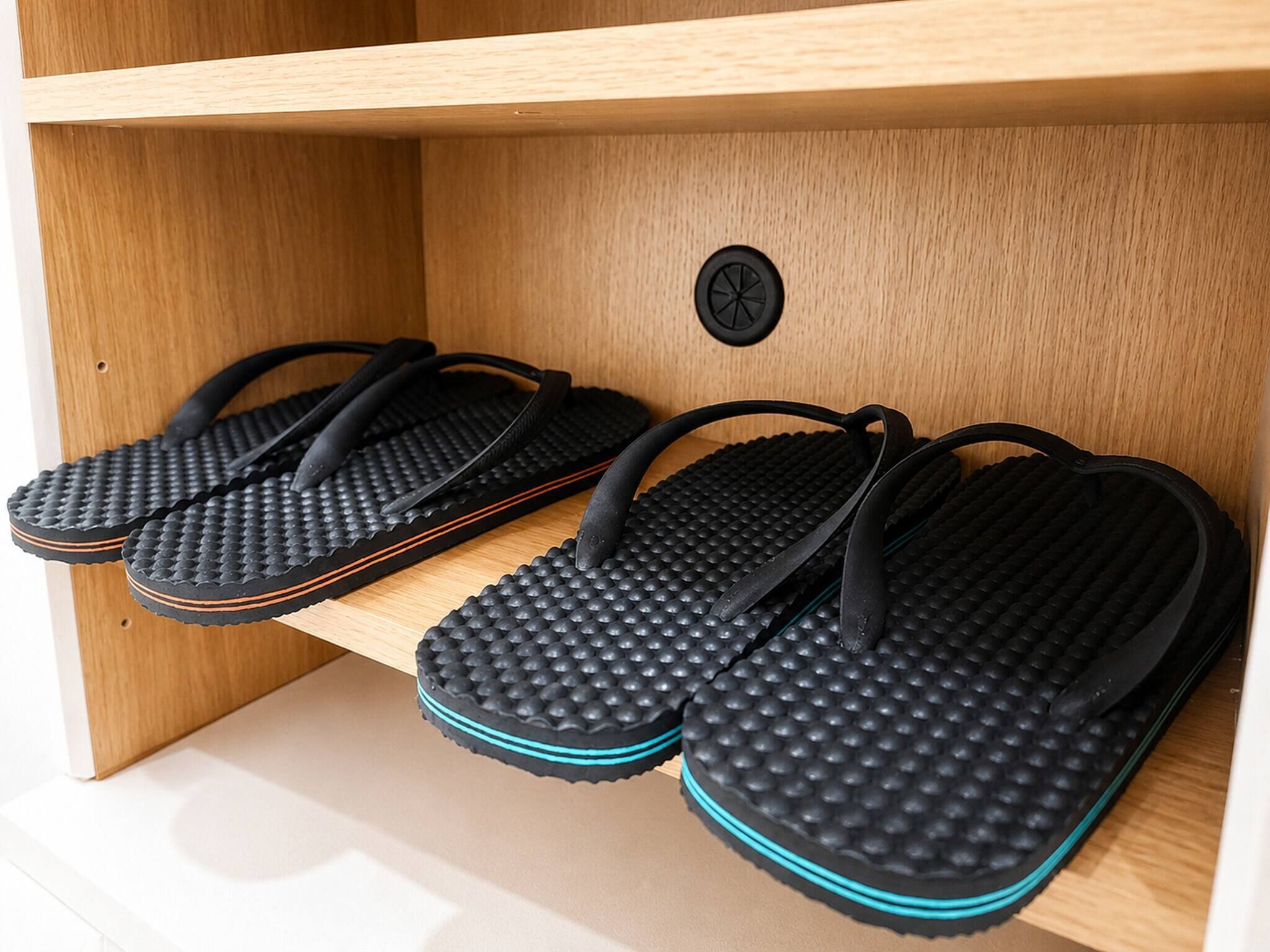 A pair of black flip-flops with textured soles on a wooden shelf.