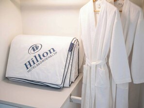 A neatly folded white pillow with the Hilton Hotels & Resorts logo on a white surface, next to a white bathrobe hanging on a rack. - S&G Beachfront Serviced 1-br, Step to Tops and 7-11 (Pattaya)