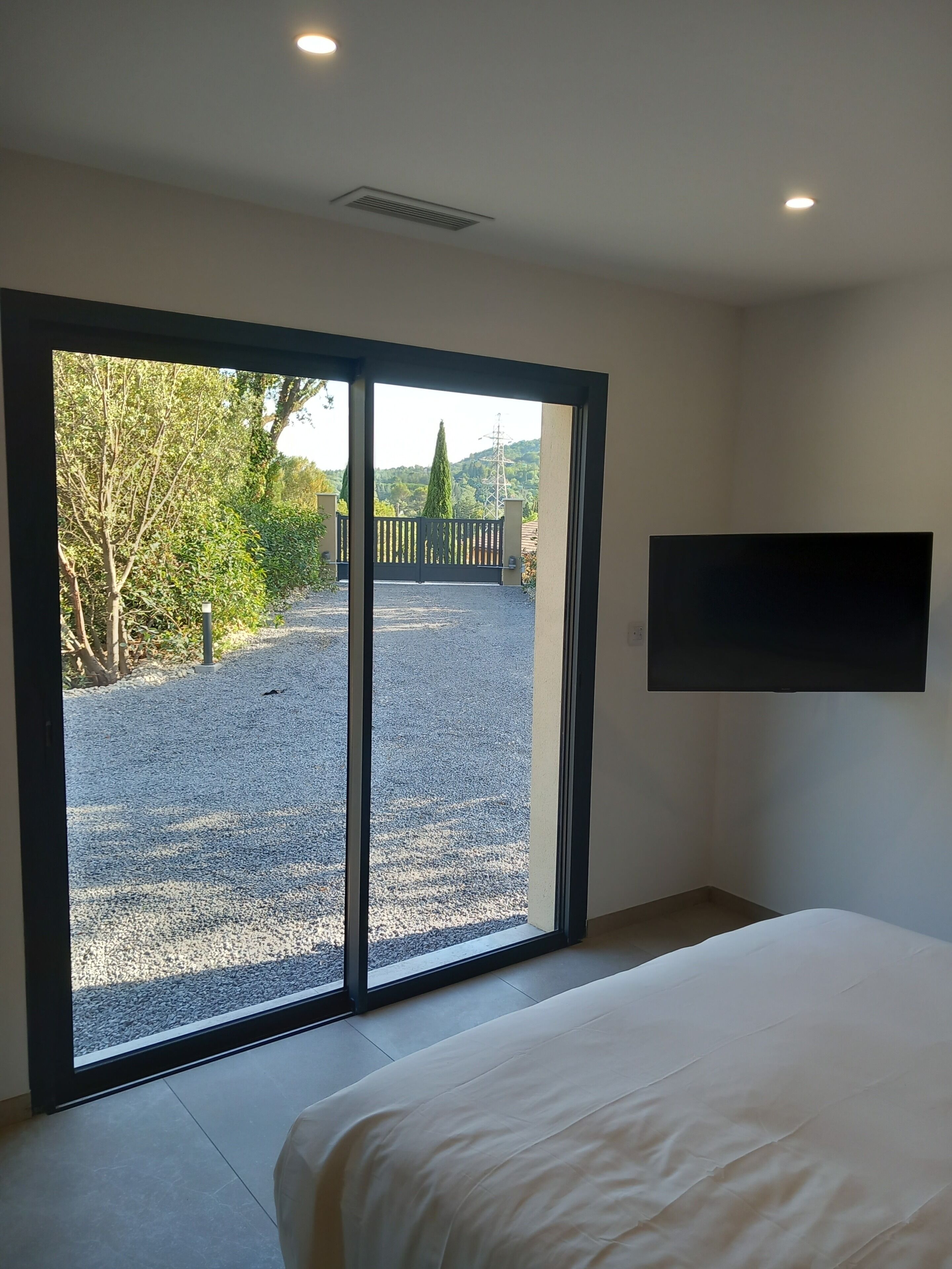 Une chambre avec un lit et une grande porte-fenêtre coulissante donnant sur un espace extérieur composé de gravier et de verdure.