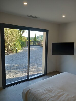 A bedroom with a bed, a large sliding glass door leading to an outdoor area with gravel and greenery.