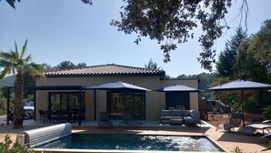 Una casa moderna con piscina, area relax all'aperto e ombrelloni.