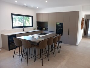 A modern kitchen with a central island, bar stools, a built-in oven, and a large window.