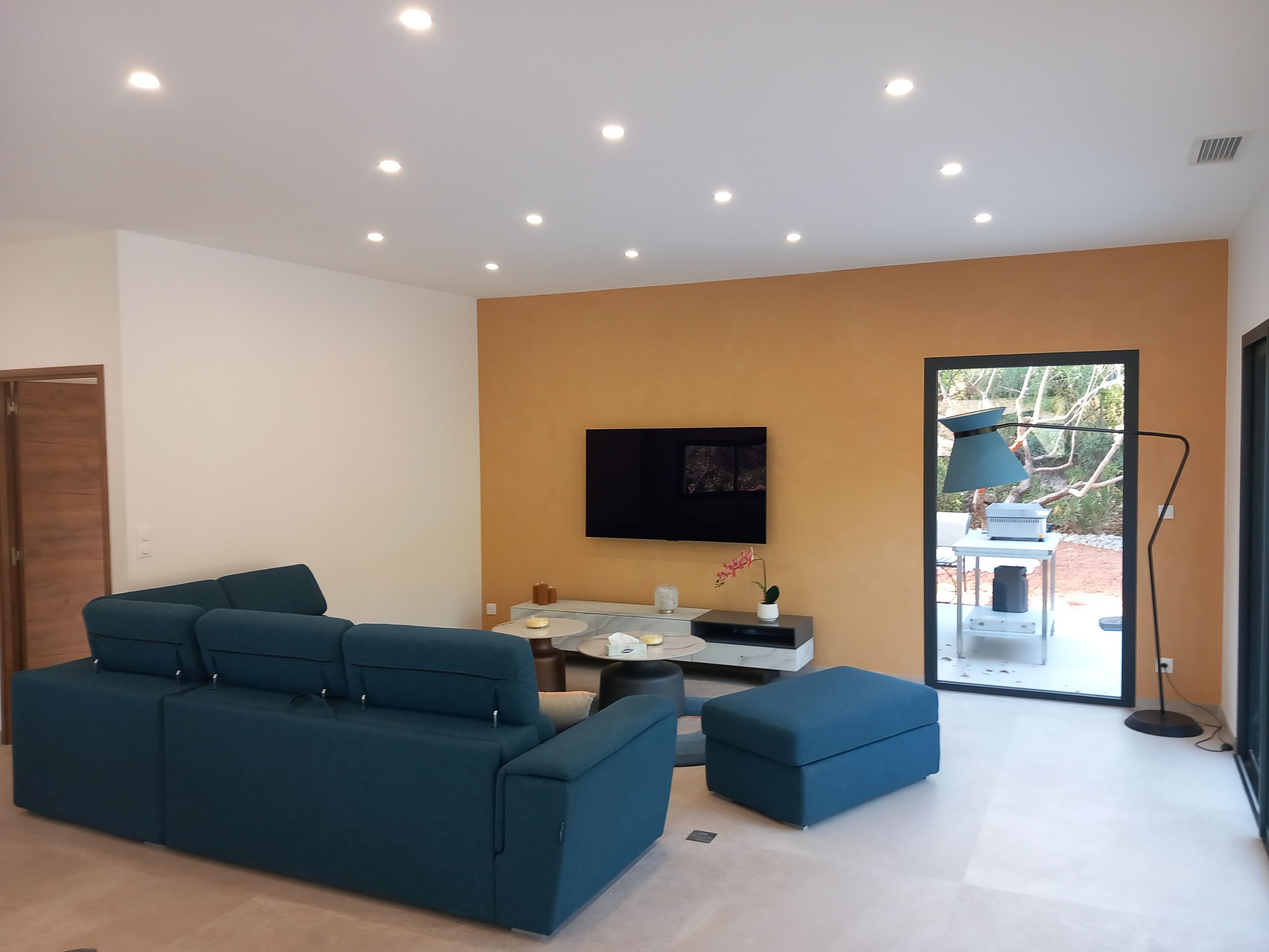Un salon moderne avec un canapé bleu, un téléviseur à écran plat fixé au mur et une petite table avec une lampe.
