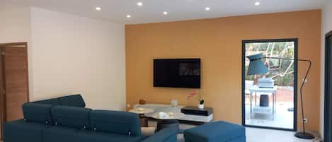 A modern living room with a blue sofa, a flat-screen TV mounted on the wall, and a small table with a lamp.