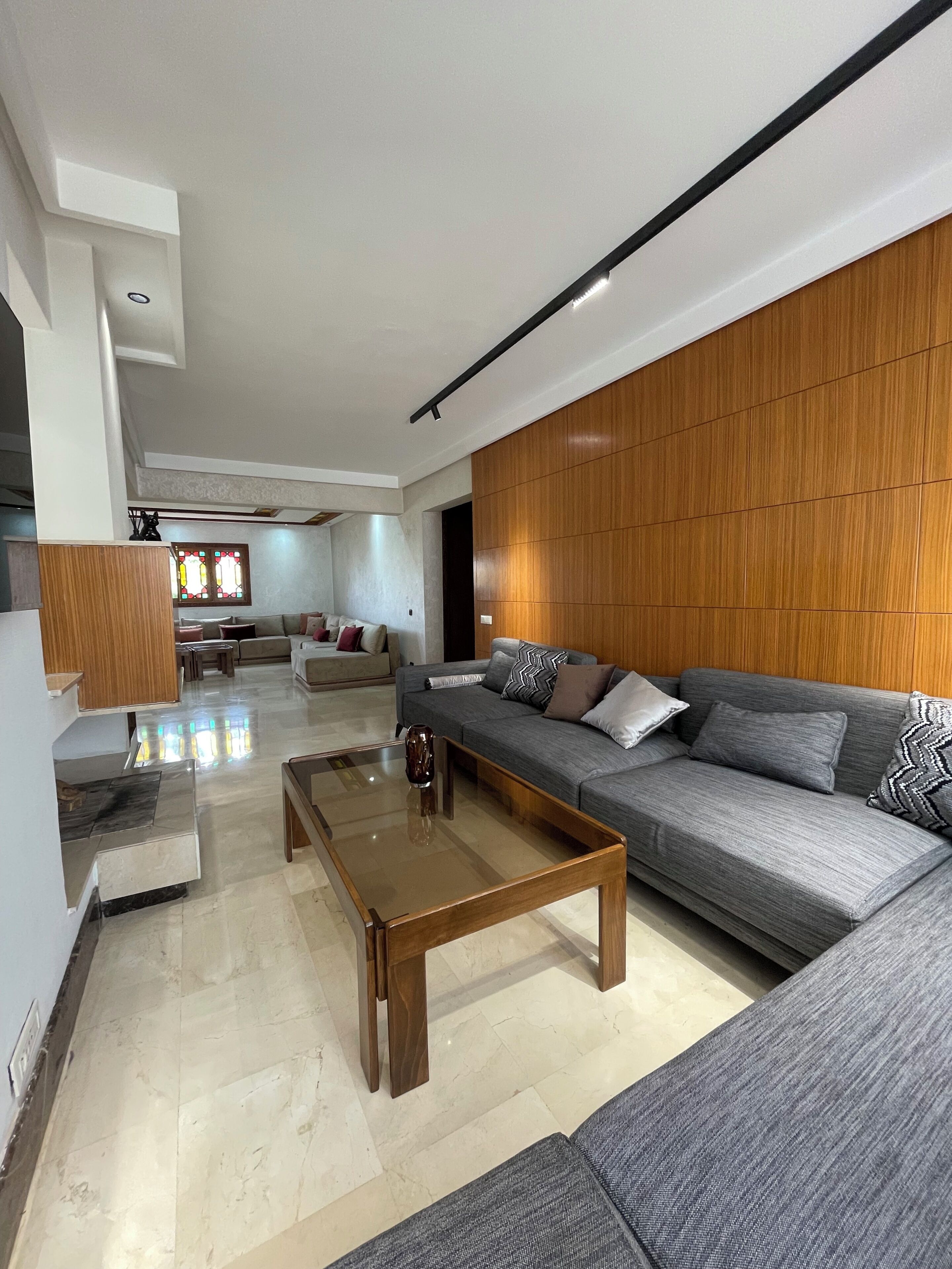 Una sala de estar moderna con un sofá gris, un panel de pared de madera y una mesa de centro de vidrio.