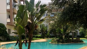 A swimming pool surrounded by greenery and a building in the background. - luxuary 3-bedroom apartment with AC in adorable Mohammédia (Mohammédia)