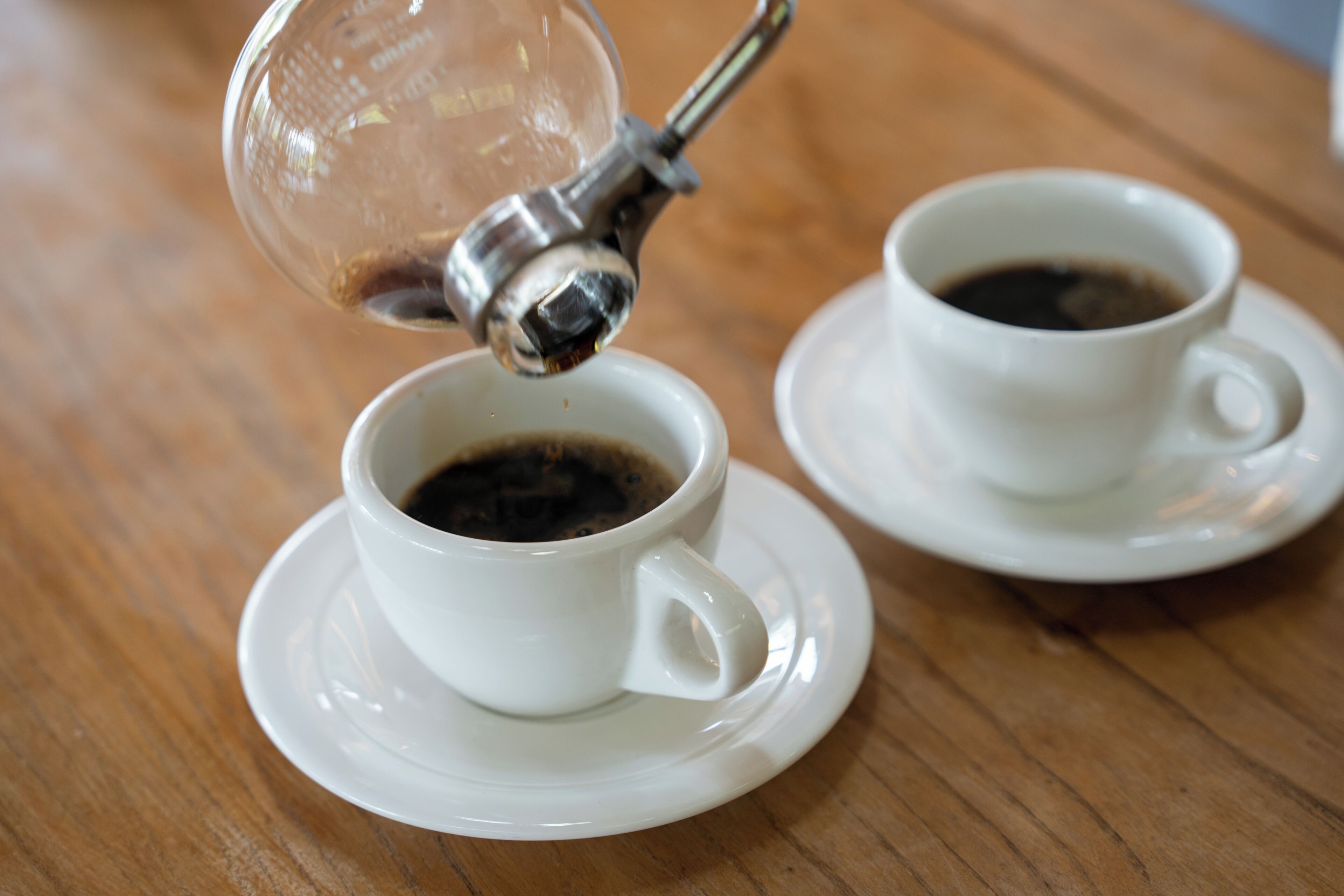 Dos tazas blancas de café sobre platillos en una mesa de madera.
