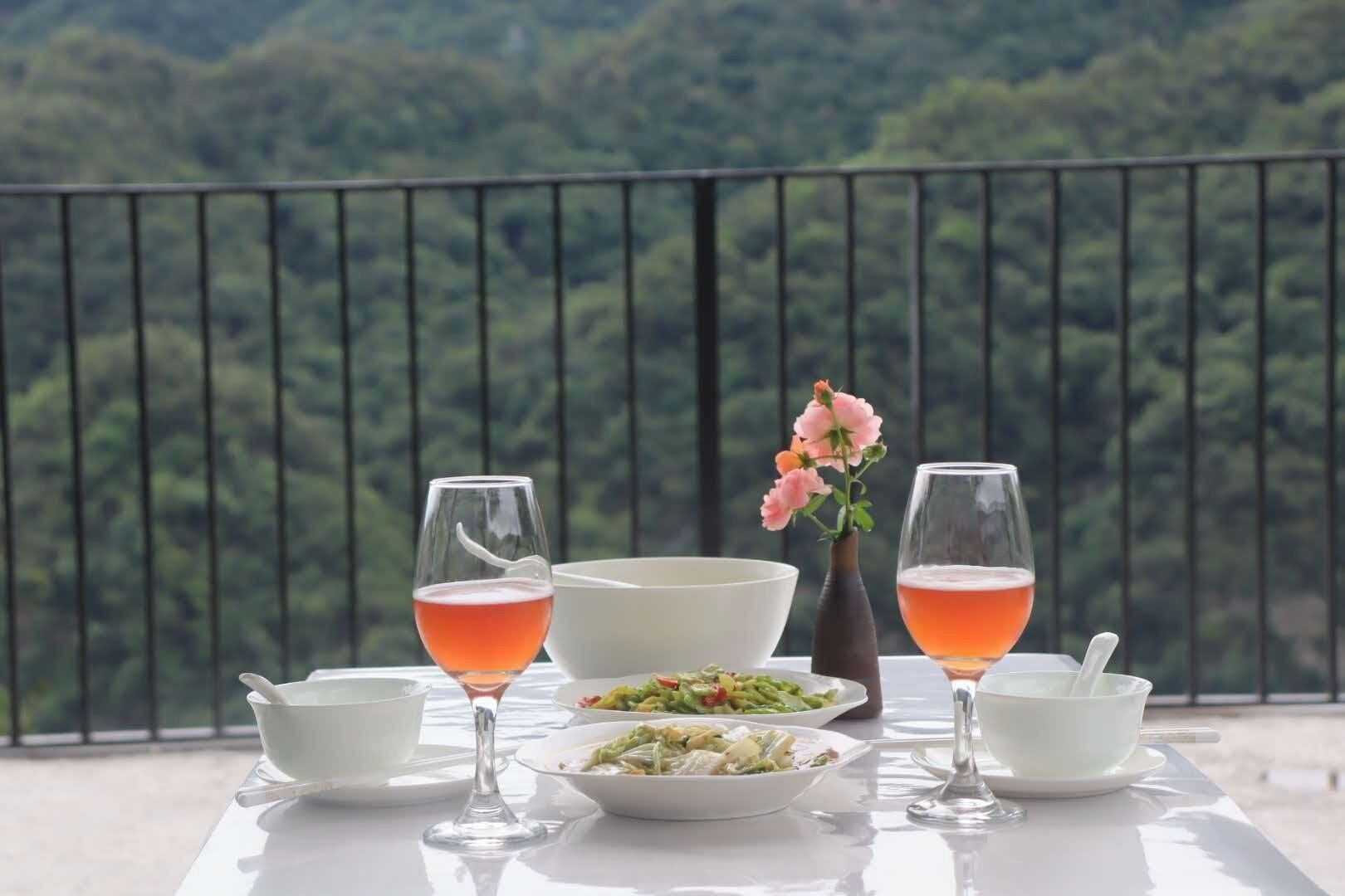 A table set with a white tablecloth, two glasses of a pink beverage, a white bowl, a vase with pink flowers, and a plate of food.