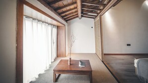 Una habitación con techo de madera, una puerta corredera, una pequeña mesa con un libro y una planta.