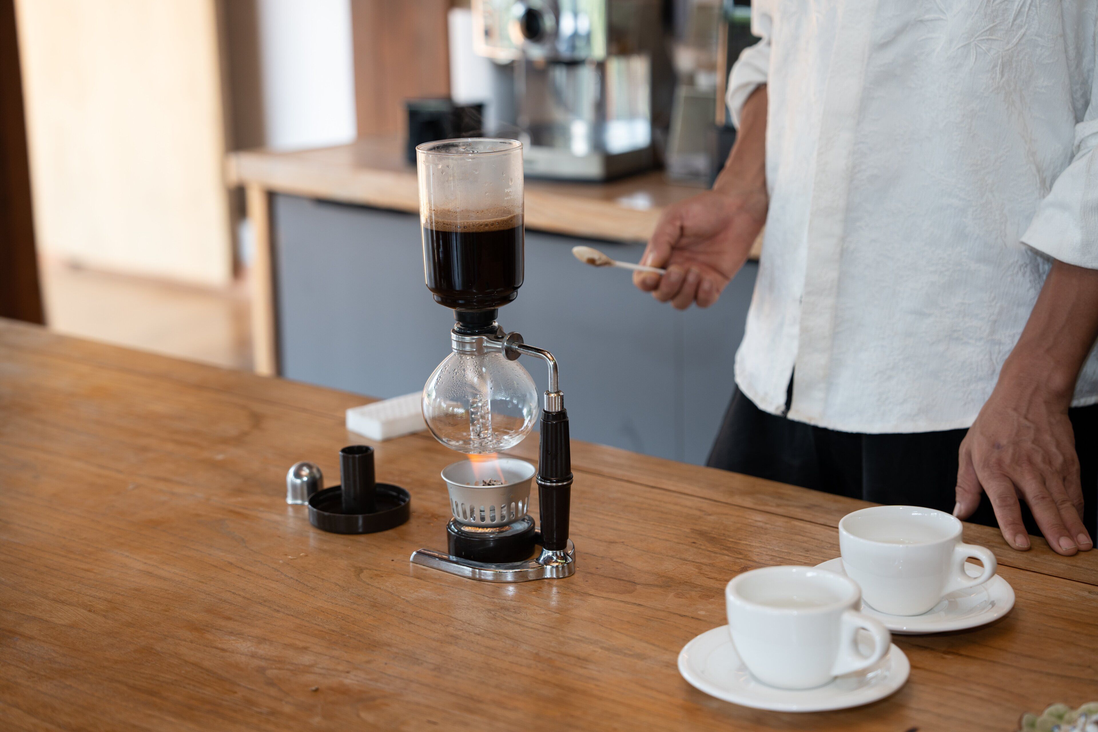 Una cafetera sobre una mesa de madera, con dos tazas y platillos blancos.
