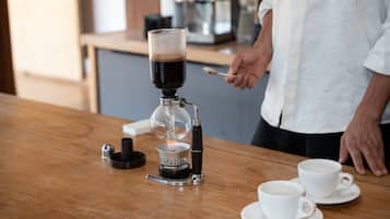 Una cafetera sobre una mesa de madera, con dos tazas y platillos blancos.