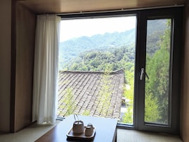 Una habitación con puerta corrediza de vidrio que da a un tejado tradicional de azulejos y abundante vegetación.