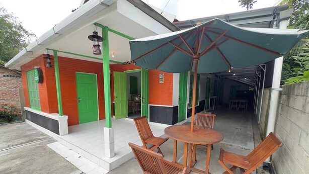 A building with a covered patio area featuring a round wooden table and four chairs. - Cozzy Joeragan Homestay (Turi)