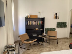 A living room with a bookshelf, two chairs, a coffee table, a TV, and a plant. - Well. St. House | Downtown - 5-minute walk to the beach - 3 bedrooms (Pescara)