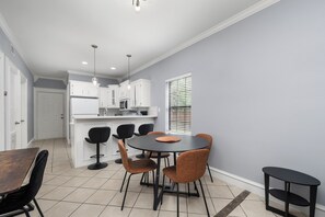 A modern kitchen with white cabinets, a black dining table with chairs, and a window with blinds. - The C2 Gateway to Starbase (Brownsville)