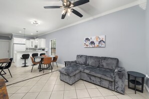 A modern living room with a sectional sofa, a dining area with a table and chairs, a kitchen with white cabinets, and a ceiling fan. - The C2 Gateway to Starbase (Brownsville)